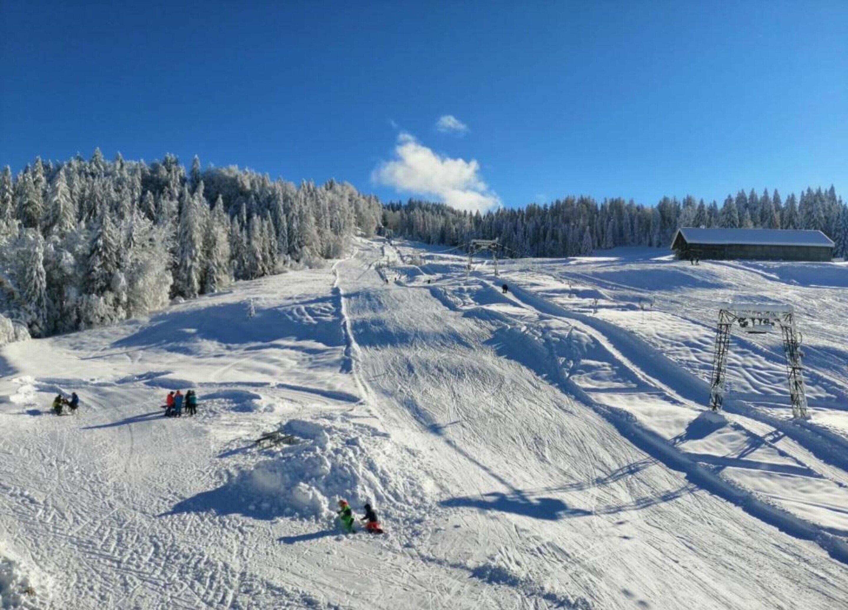 A snowy ski slope with a clear sky, a wooden cabin, and a forest in the background.
