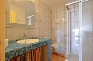 Un baño con suelo de baldosas, lavamanos, inodoro y ducha.