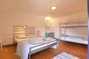 Un dormitorio con una cama individual, una cama litera, piso de madera, una mesita de noche y un mueble pequeño.