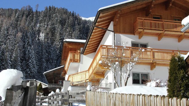 A wooden chalet with a balcony, surrounded by snow-covered trees and a wooden fence. - Cozy Apartment in Ausservillgraten (Ausservillgraten)