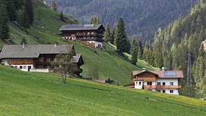 A hillside with traditional wooden houses, some with balconies and solar panels, surrounded by lush greenery and mountains. - Cozy Apartment in Ausservillgraten (Ausservillgraten)