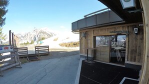 Ein Holzgebäude mit einem Schild, auf dem "Café Services" steht, und Blick auf verschneite Berge im Hintergrund.