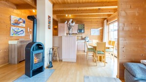 Ein gemütliches Blockhäuschen mit Kaminofen, Holzwänden, Essbereich und einer Küche.