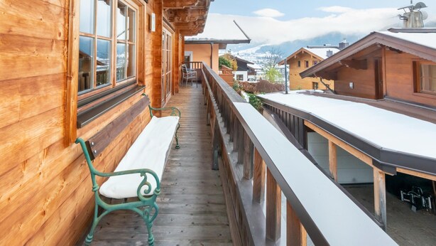 Ein Holzbalkon mit einer Bank und Blick auf schneebedeckte Berge.