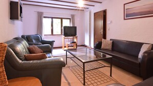 A living room with a glass coffee table, two leather sofas, a television on a stand, and a painting on the wall.