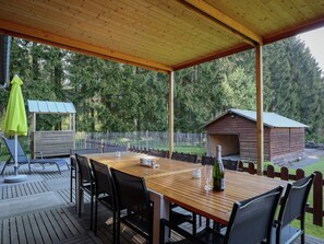A covered outdoor seating area with a wooden table and chairs, a small gazebo, and a wooden cabin in a wooded setting. - Holiday Home in Recht With Garden (Sankt-Vith)