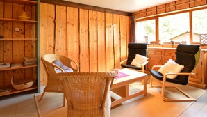 A cozy room with wooden walls, a wicker chair, a black chair, and a small table.