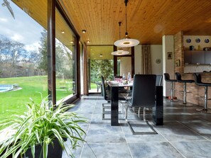 A spacious dining area with a view of a swimming pool, large windows, and a modern kitchen with bar stools.