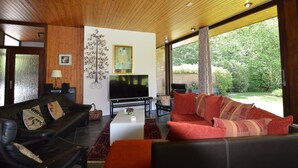 A modern living room with a wooden ceiling, a flat-screen TV, a red sofa, a black leather couch, and a coffee table. - Luxury Villa with Swimming Pool near F1 Circuit (Stavelot)
