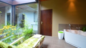 A modern bathroom with a glass shower enclosure, a white bathtub, and a small bedside table with a green cushion. - Luxury Villa with Swimming Pool near F1 Circuit (Stavelot)