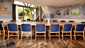 Un salón de conferencias con una larga mesa de madera, sillas tapizadas en azul y una escalera que da a un espacio al aire libre.