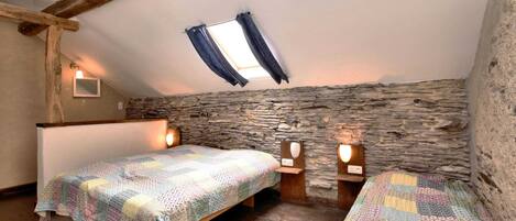 A cozy attic bedroom with two beds, wooden beams, stone walls, and a sloped ceiling.