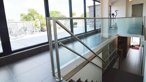 A modern interior with a glass railing, a staircase, and large windows offering a view of outdoor seating. - Family Villa, Profondeville (Profondeville)