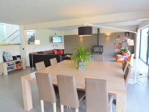 Een moderne woonkamer met een eethoek, met een houten tafel, lederen stoelen, een potplant en een televisie aan de muur.