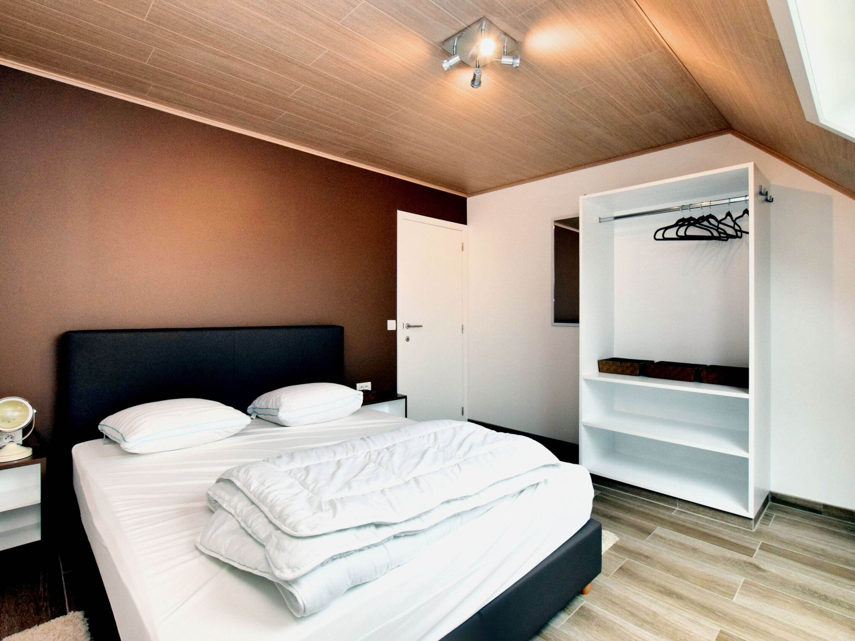 A modern bedroom with a bed, a wardrobe, and a ceiling light fixture.