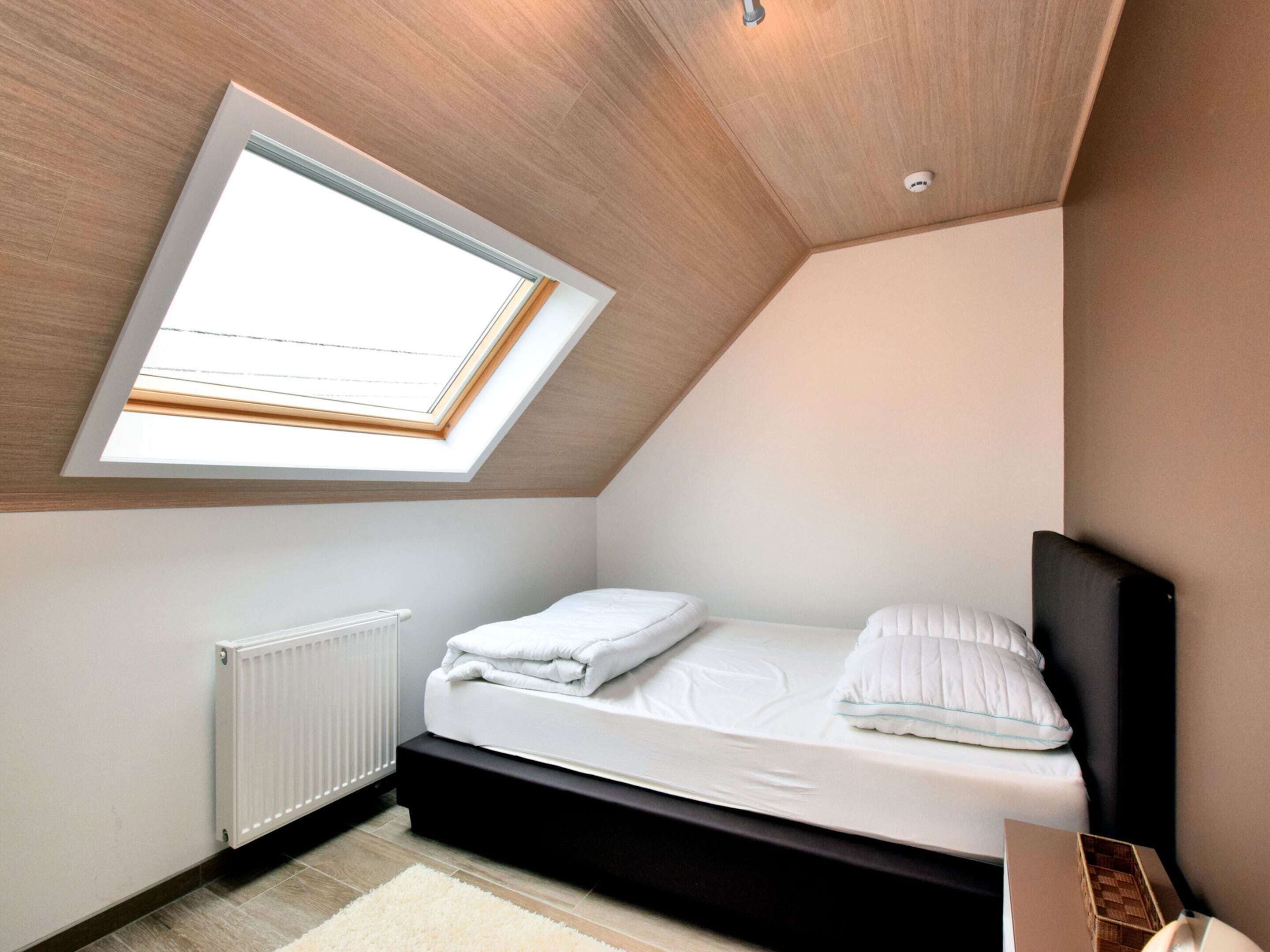 Une petite chambre à coucher moderne, dotée d’une lucarne, d’un lit, d’un radiateur et d’un plancher en bois.