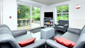 A modern living room with grey sofas, a flat-screen TV, and a bookshelf. - Luxurious Home With Sauna (Somme-Leuze)