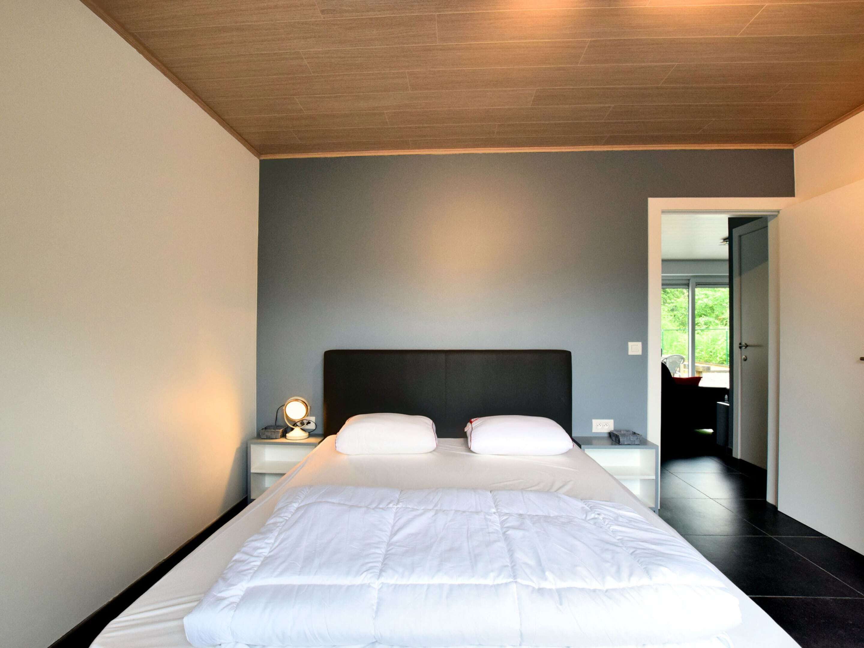 Een moderne slaapkamer met een groot bed, een nachtkastje en een spiegel.