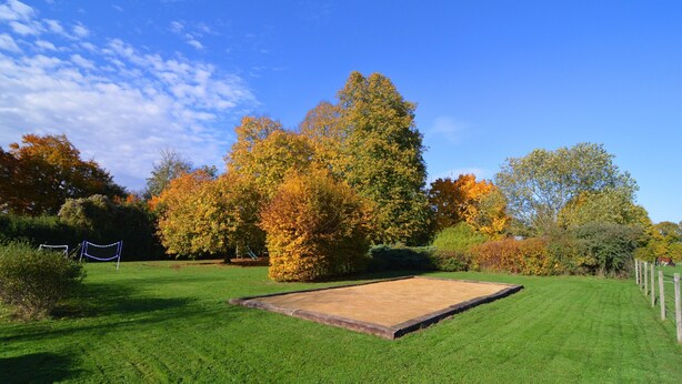 A well-maintained lawn with a rectangular area, possibly for sports or gatherings, surrounded by trees with autumn foliage. - Spacious Holiday Home With Private Garden (Houyet)