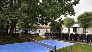 An outdoor table tennis table with chairs, surrounded by greenery and a building in the background. - Spacious Holiday Home With Private Garden (Houyet)