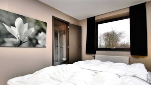Ein Schlafzimmer mit Bett, Fenster, Heizkörper und einer Tür zu einem Badezimmer.