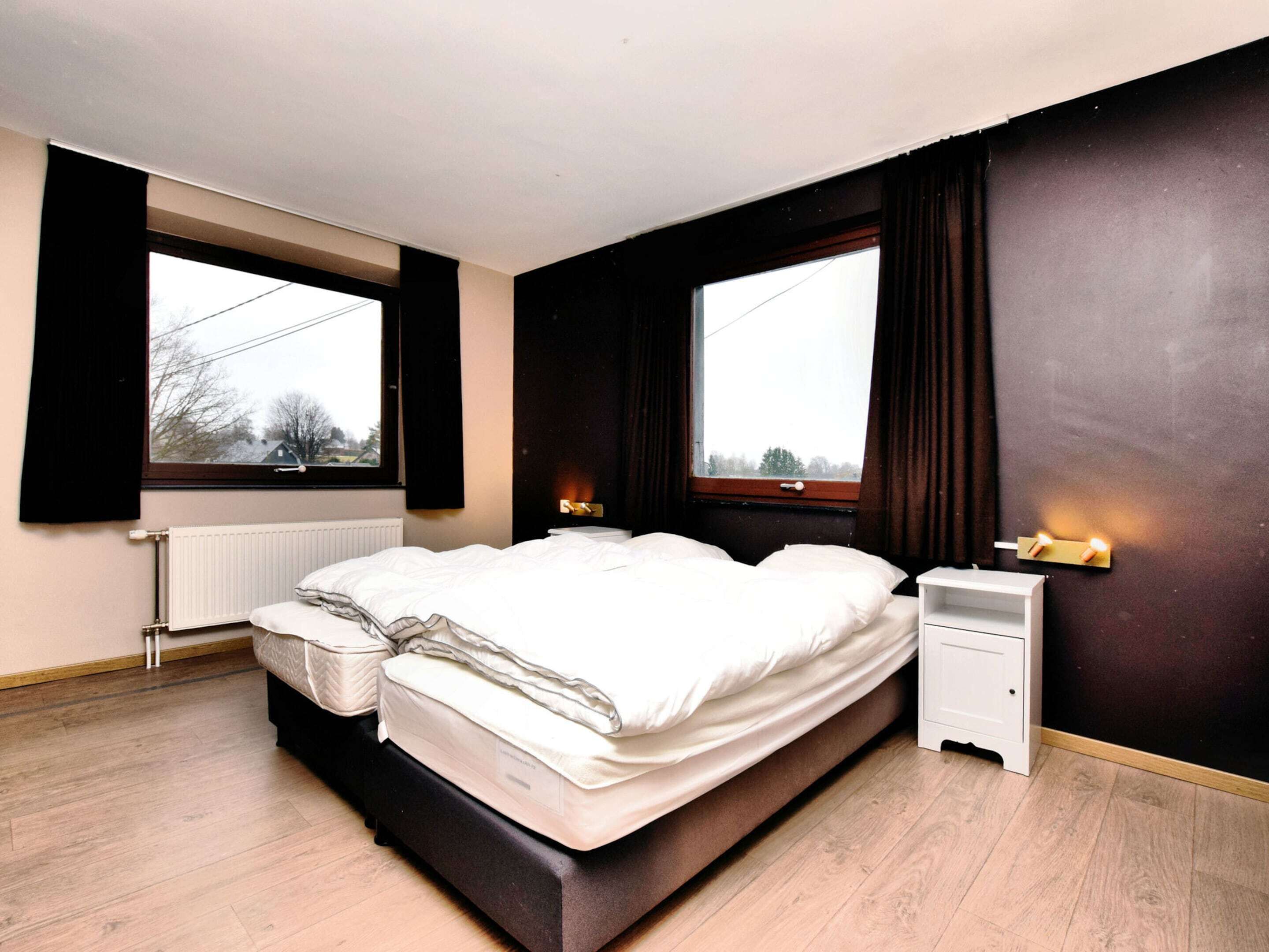 A bedroom with two beds, a radiator, a nightstand, and a window with curtains.