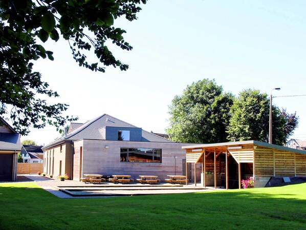 A modern building with a sloped roof, large windows, and a covered outdoor seating area with wooden tables. - Unique Holiday Home with Pool near Park & Ski Area (Malmedy)