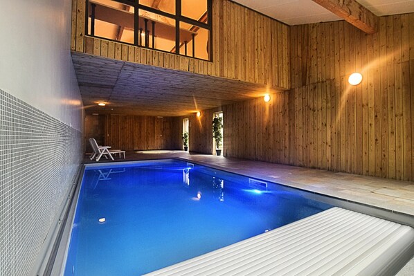 An indoor swimming pool with wooden walls and a balcony overlooking the pool.