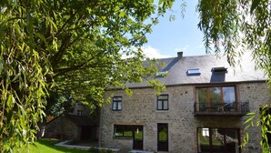 Une maison en pierre avec un balcon, une cour verdoyante et un arbre au premier plan.