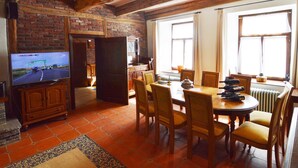 Un coin repas avec un mur en briques, des poutres en bois, un téléviseur et une table dressée pour quatre personnes.