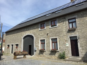 Un bâtiment en pierre doté de nombreuses fenêtres, dont certaines sont ornées de jardinières, une grande entrée en arc de cercle et des panneaux solaires sur le toit.