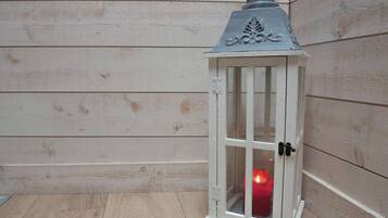 Une lanterne blanche contenant une bougie, posée sur un plancher en bois, contre un mur en bois.