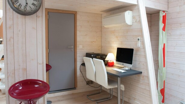 A compact room with a wooden interior, a desk with a computer, a chair, a red stool, and a wall clock. - Beautiful Apartment in Spa Belgium with Hot Tub (Spa)