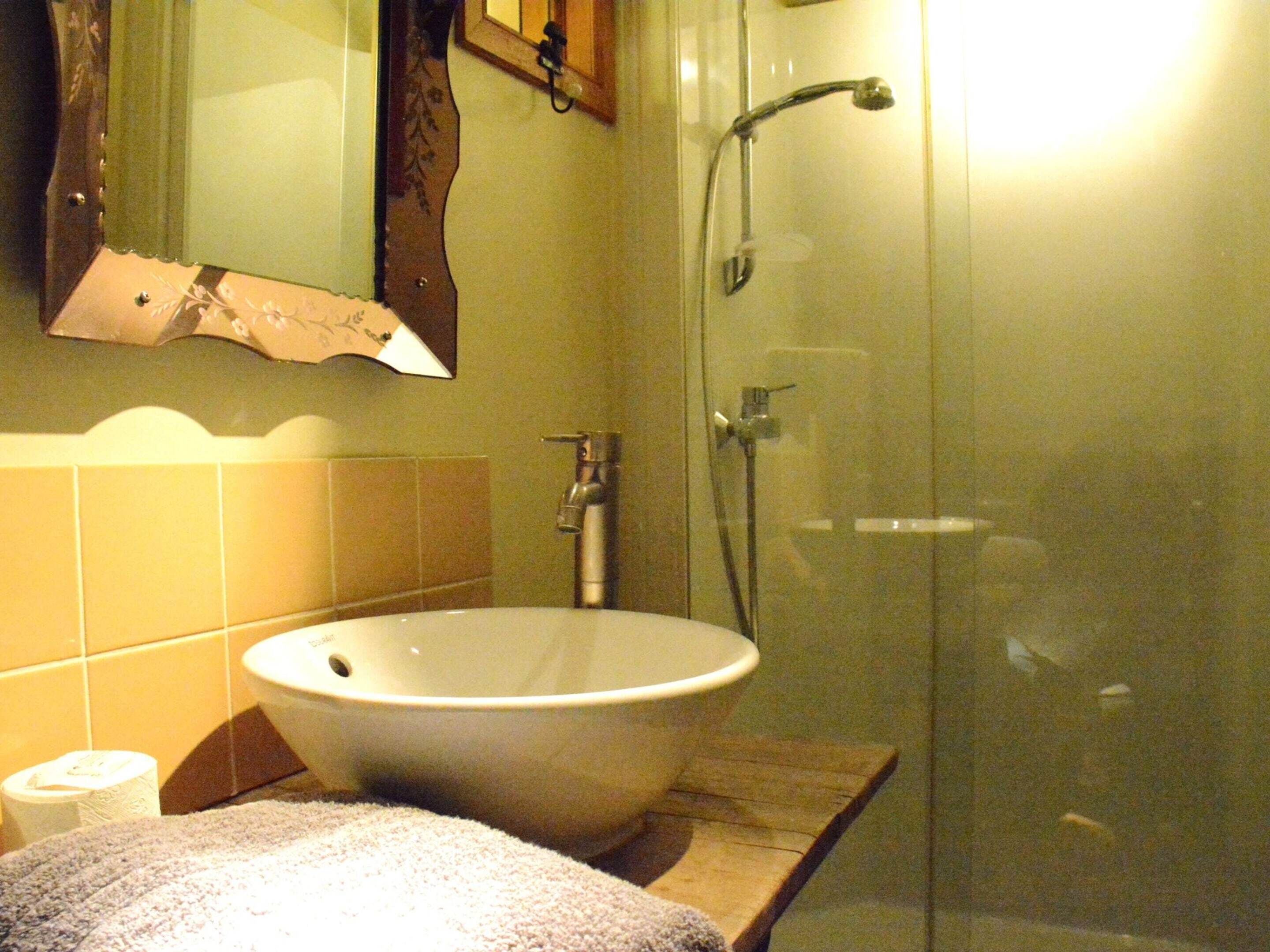 Une salle de bain avec une douche à parois de verre, un lavabo blanc et une serviette posée sur un plan de travail en bois.