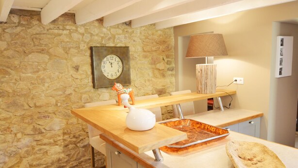 A kitchen with a stone wall, a wooden counter, a clock, a lamp, and a small decorative horse figurine. - Holiday Home in Ardennes Near Chimay Abbey (Viroinval)