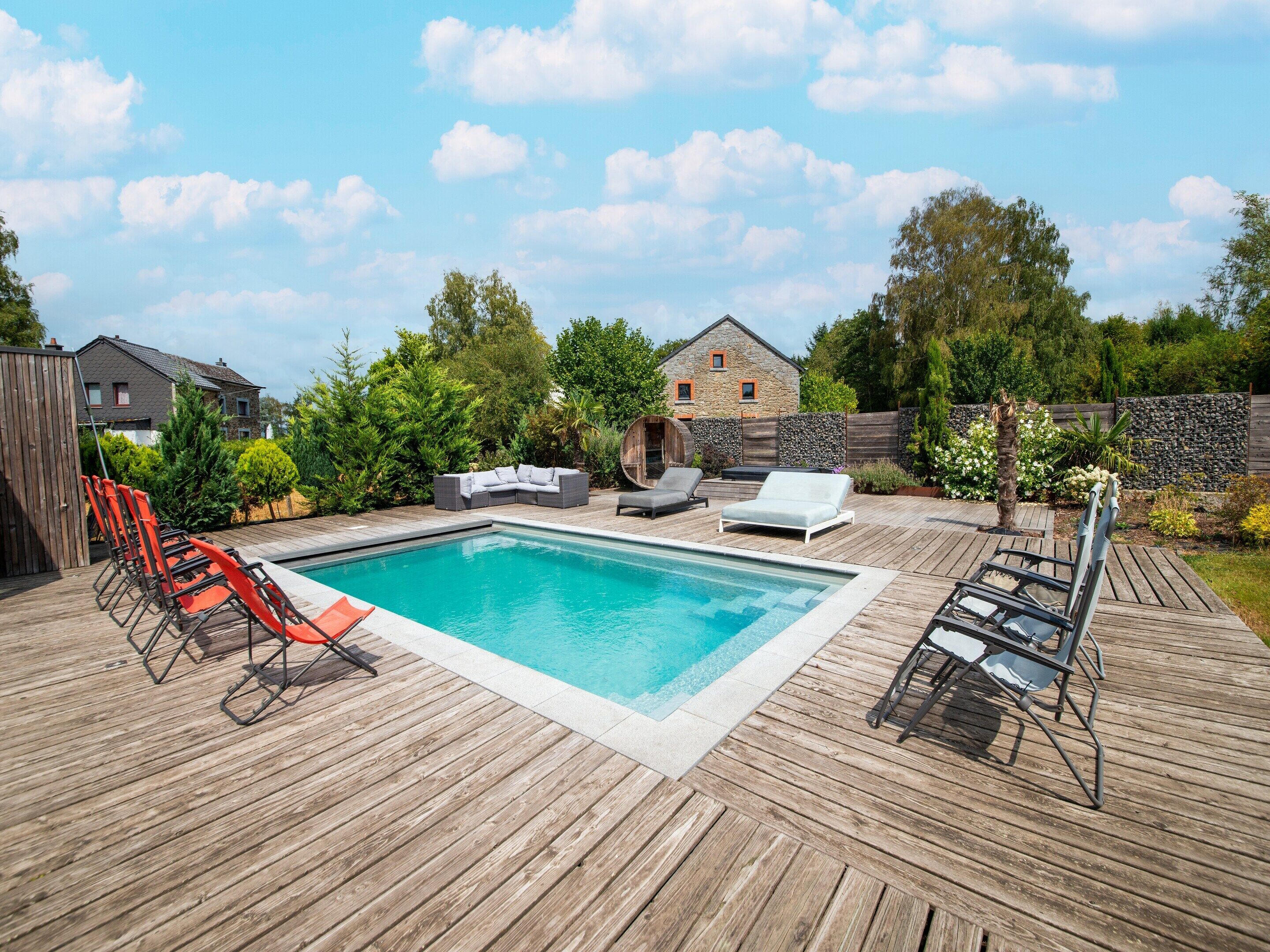 Une terrasse en bois avec une piscine, du mobilier d’extérieur et, au fond, une maison en pierre.