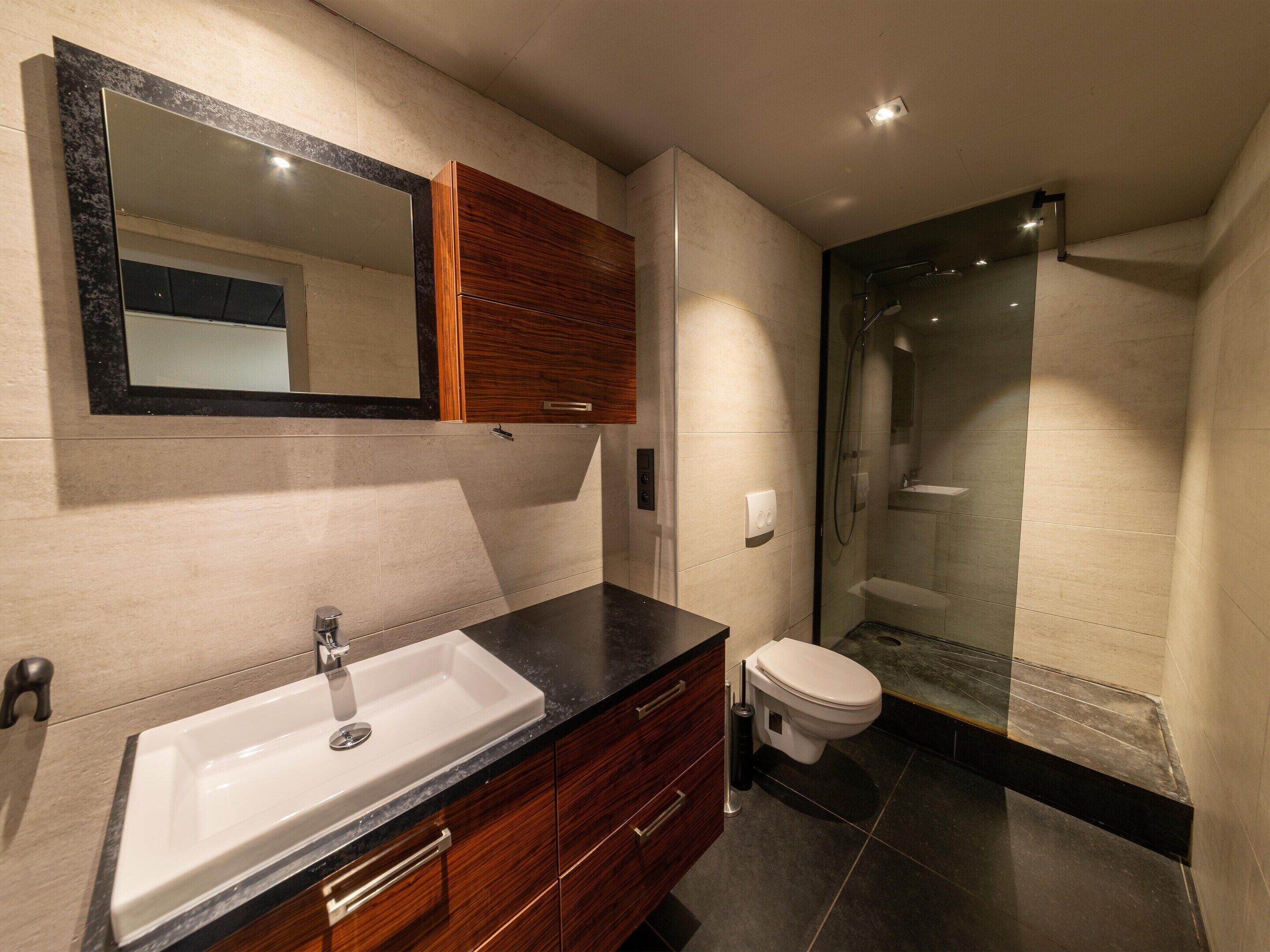 A modern bathroom with a vanity, sink, mirror, and a glass-enclosed shower area.