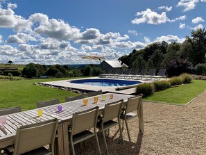 A poolside area with a table and chairs, a covered seating area, and a view of the countryside.
