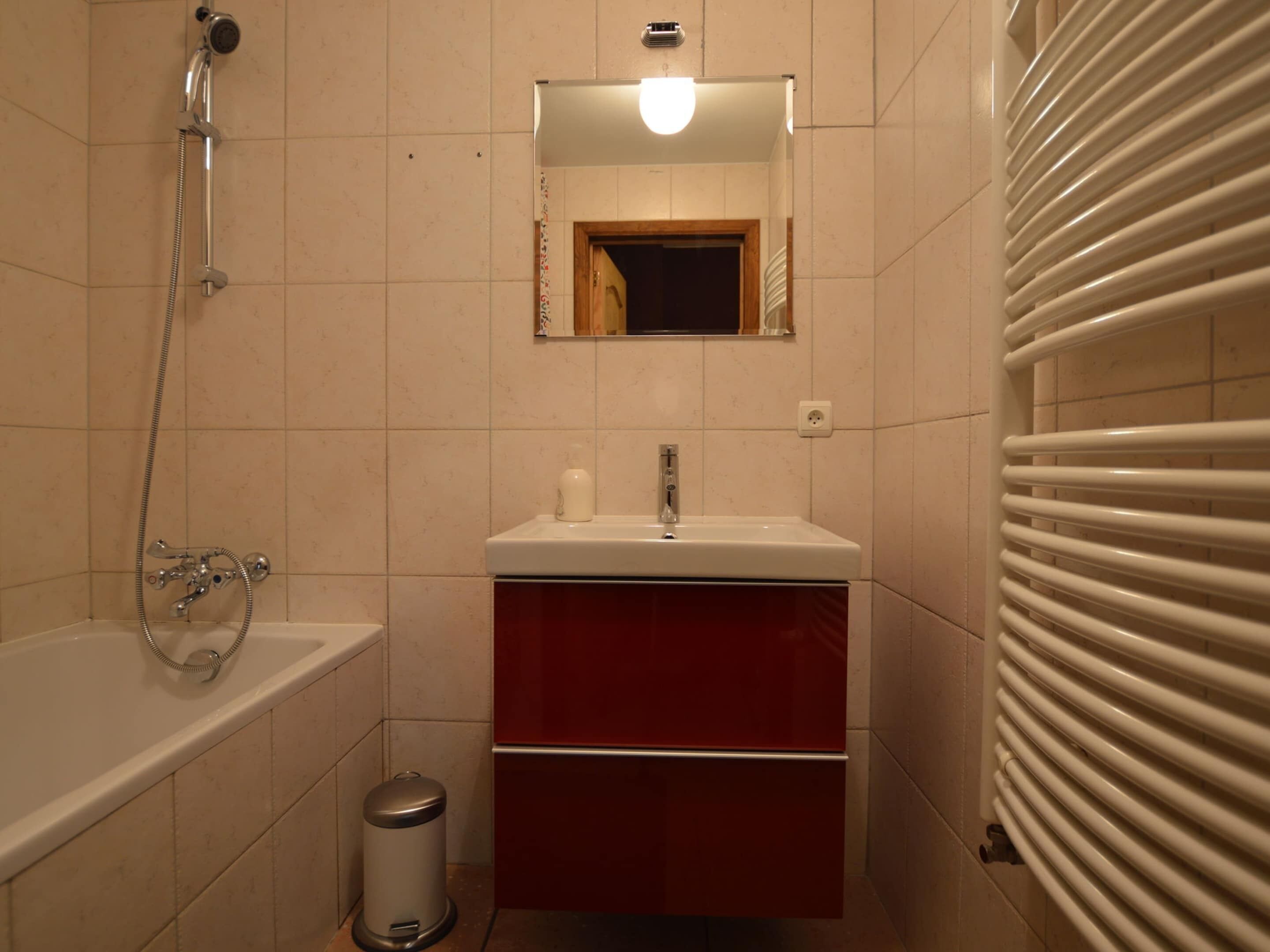 Ein Badezimmer mit einer Badewanne, einem Waschbecken, einem Spiegel und einem Heizkörper.