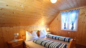 A wooden cabin bedroom with a bed, bedside tables, and a window with curtains.