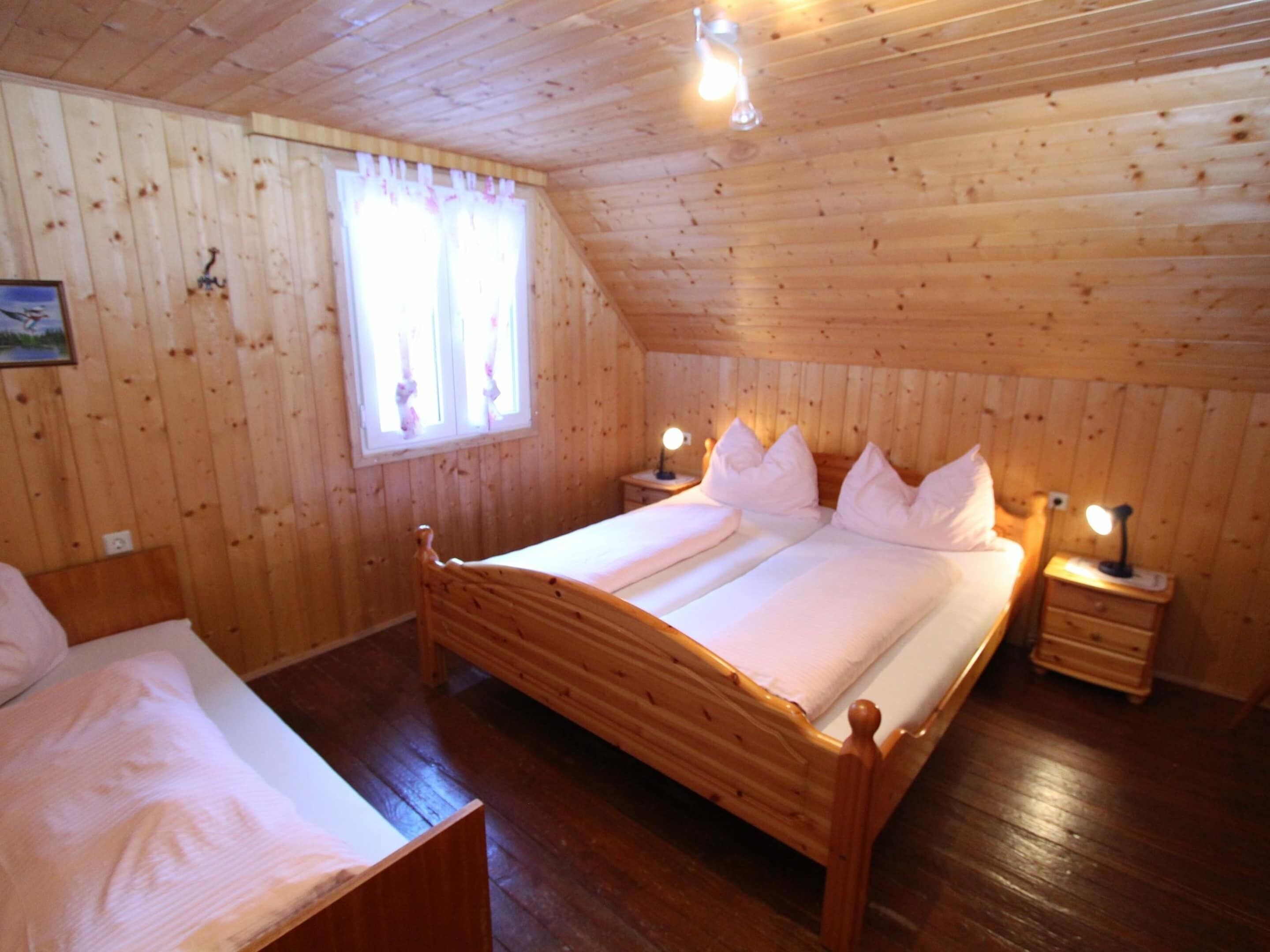 Una habitación con paneles de madera, una cama doble, dos mesitas de noche con lámparas, una ventana con cortinas y un cuadro enmarcado en la pared.