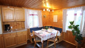 A wooden cabin interior with a dining table set for four, wooden cabinets, and a window with curtains.