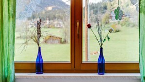 Uma janela com dois vasos azuis no parapeito, com vista para uma paisagem verde e uma casa ao longe.