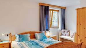 Quarto com cama de madeira, mesa de cabeceira, guarda-roupa e janela com cortinas.