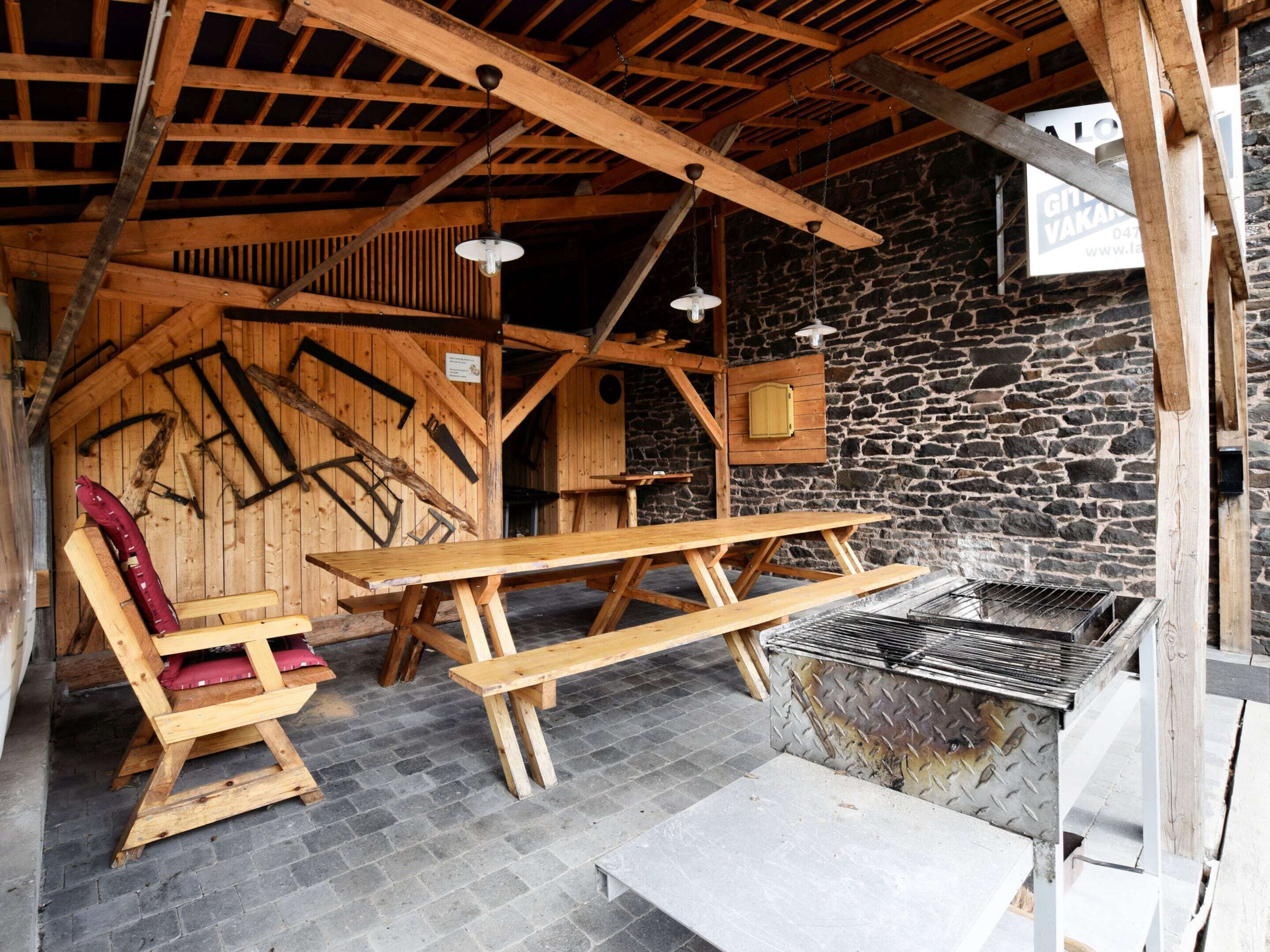 Une cabane rustique en bois, dotée d’un mur en pierre, d’un banc en bois, d’une table de pique-nique et d’un barbecue.