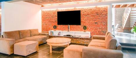 A modern living room with a brick wall, a flat-screen TV, and a staircase in the background.