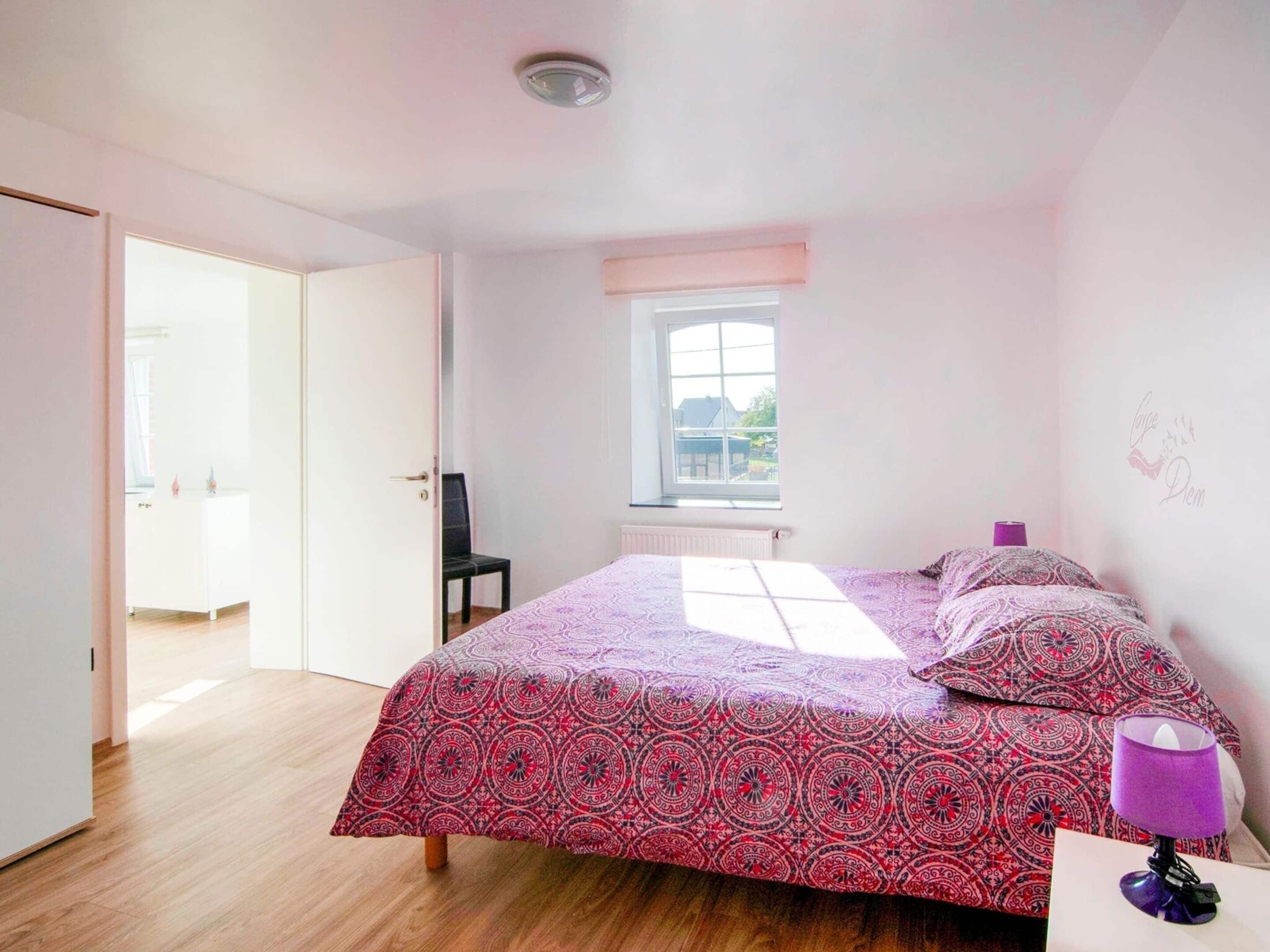 Een slaapkamer met een bed, een stoel, een raam en een deur die naar een andere kamer leidt.
