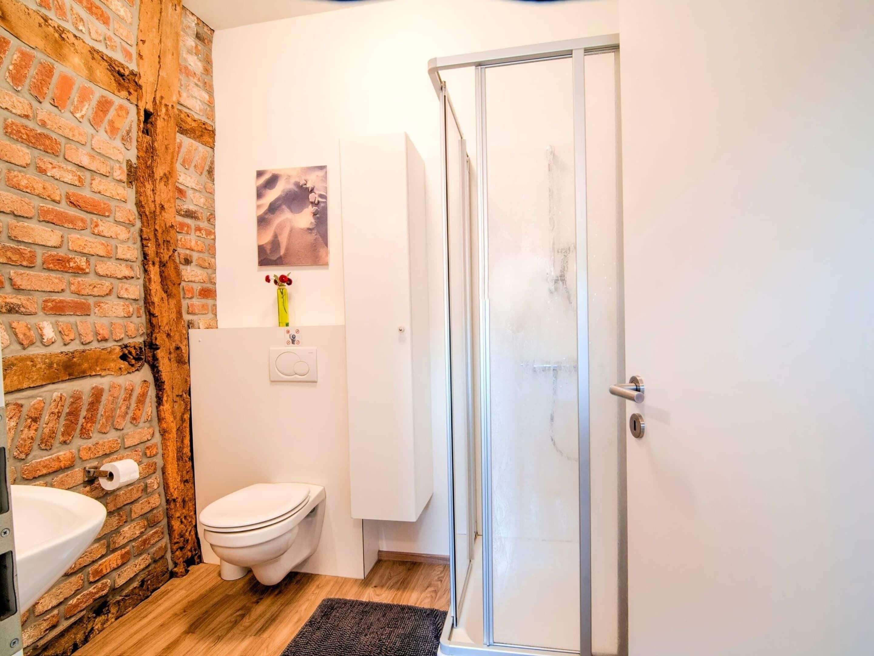 A bathroom with a brick wall, a toilet, a sink, a shower, and a door.