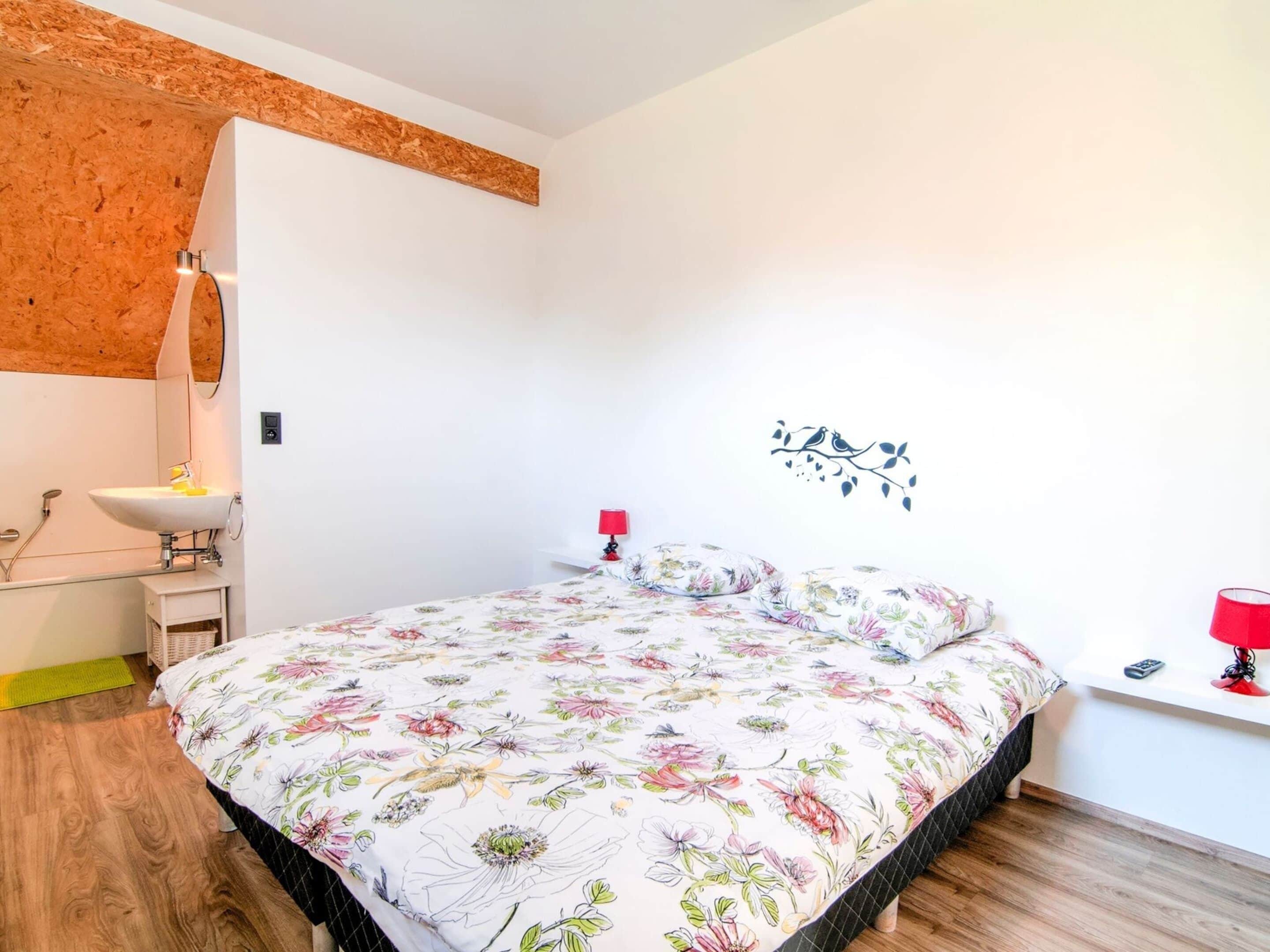 A bedroom with a floral bedspread, a white sink, a red lamp, and a wall-mounted bird decoration.