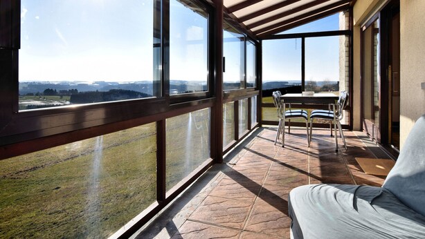Ein Balkon mit Tisch und Stühlen, großen Fenstern und Blick auf die Landschaft.